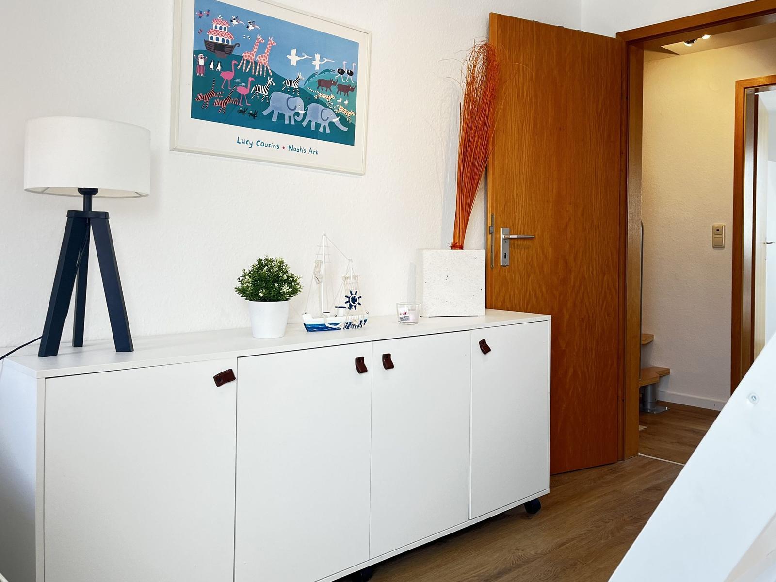 Weißer Schrank mit Dekoration, Wandbild Noahs Arche und Tür im Hintergrund.