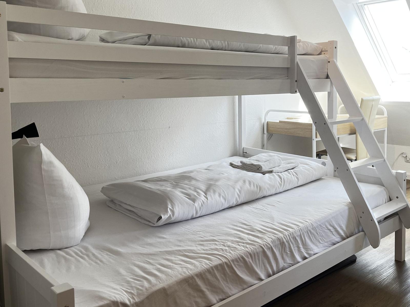 Ein weißes Doppelstockbett mit Matratzen und Bettwäsche. Eine Leiter führt zur oberen Etage.
