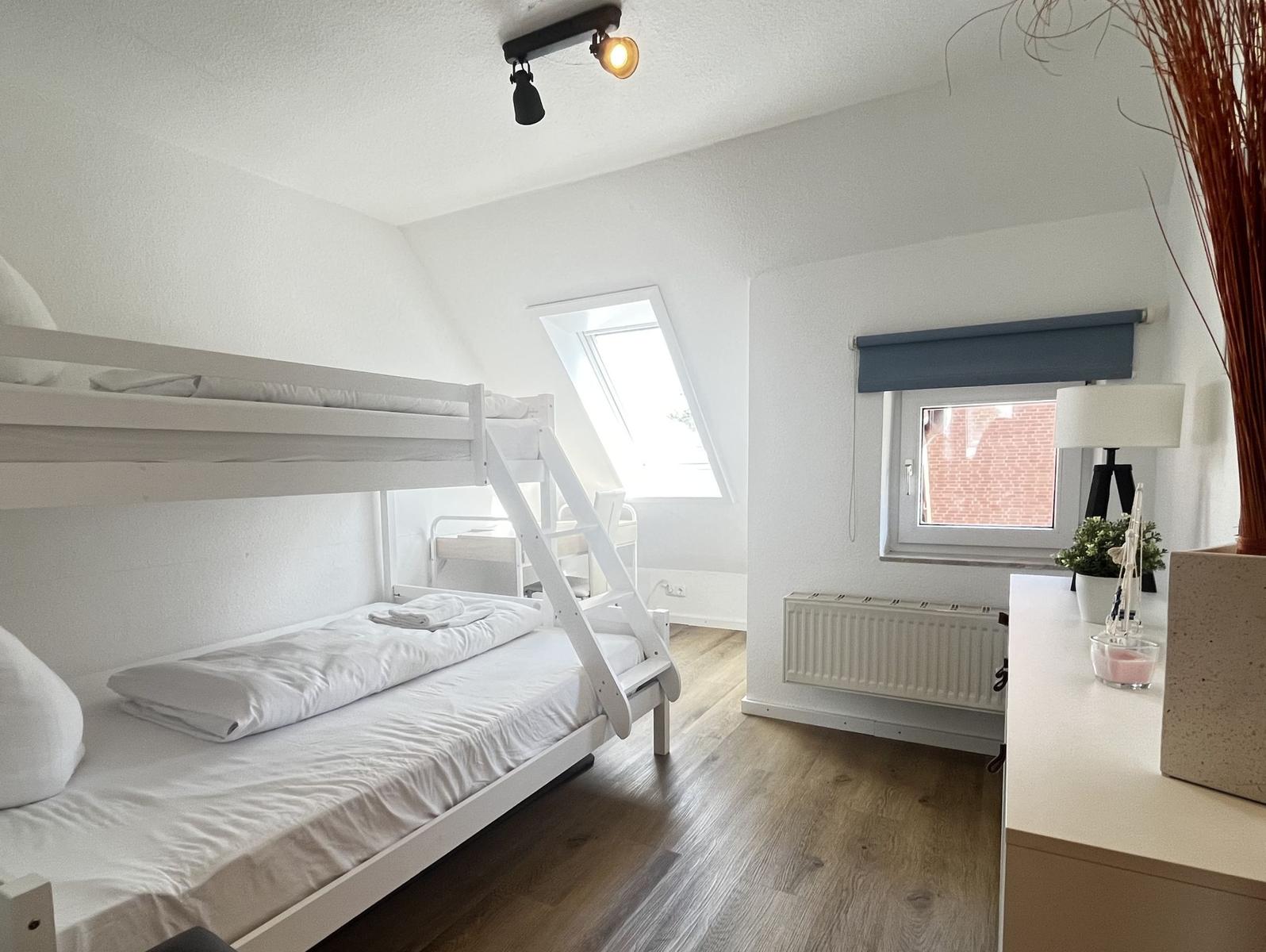 Zimmer mit Doppelstockbett, Holzboden und Dachfenster. Fenster mit Rollladen und Schreibtisch.