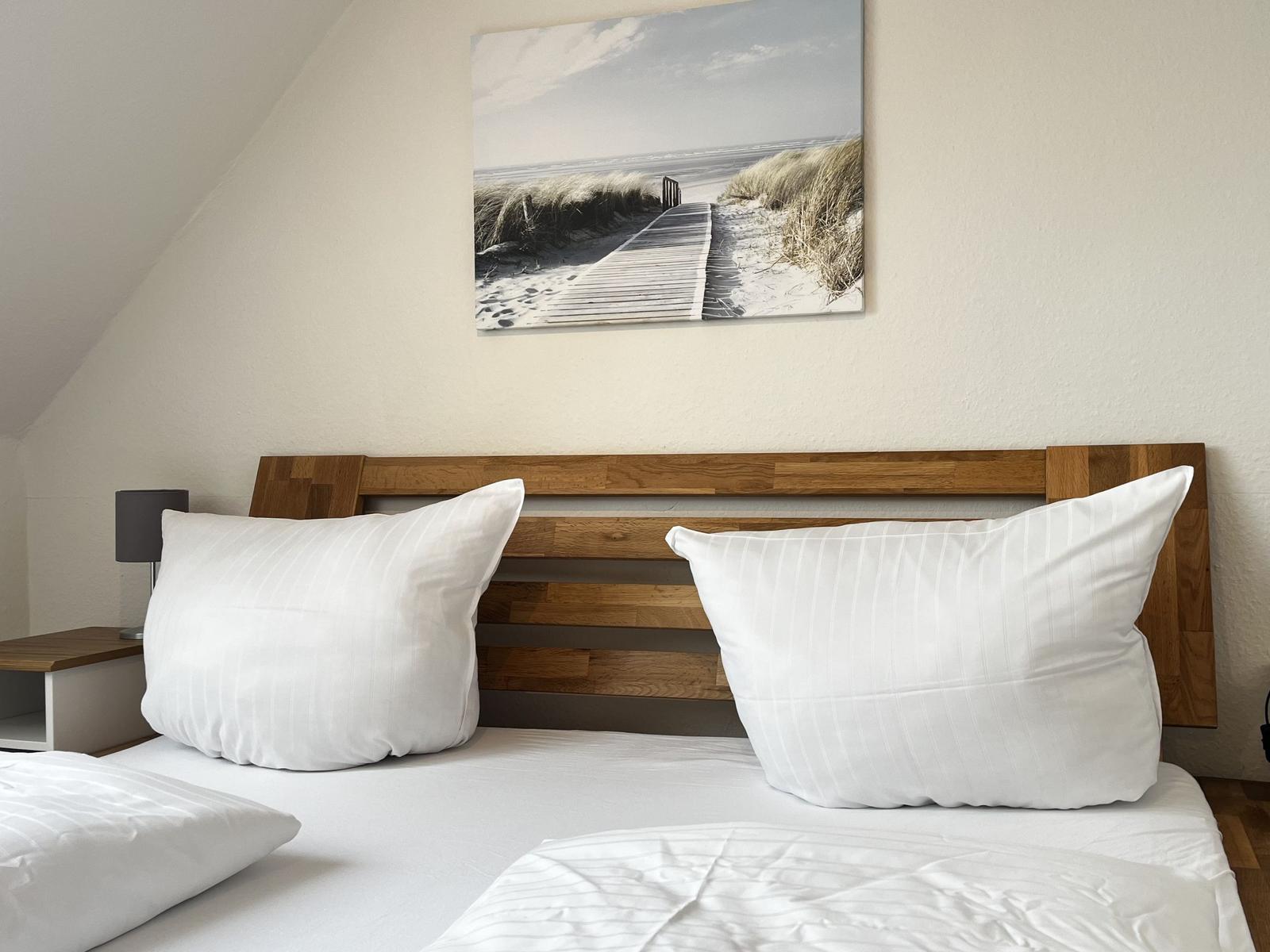 Schlafzimmer mit Holzbett, weißen Kissen und Strandbild an der Wand.