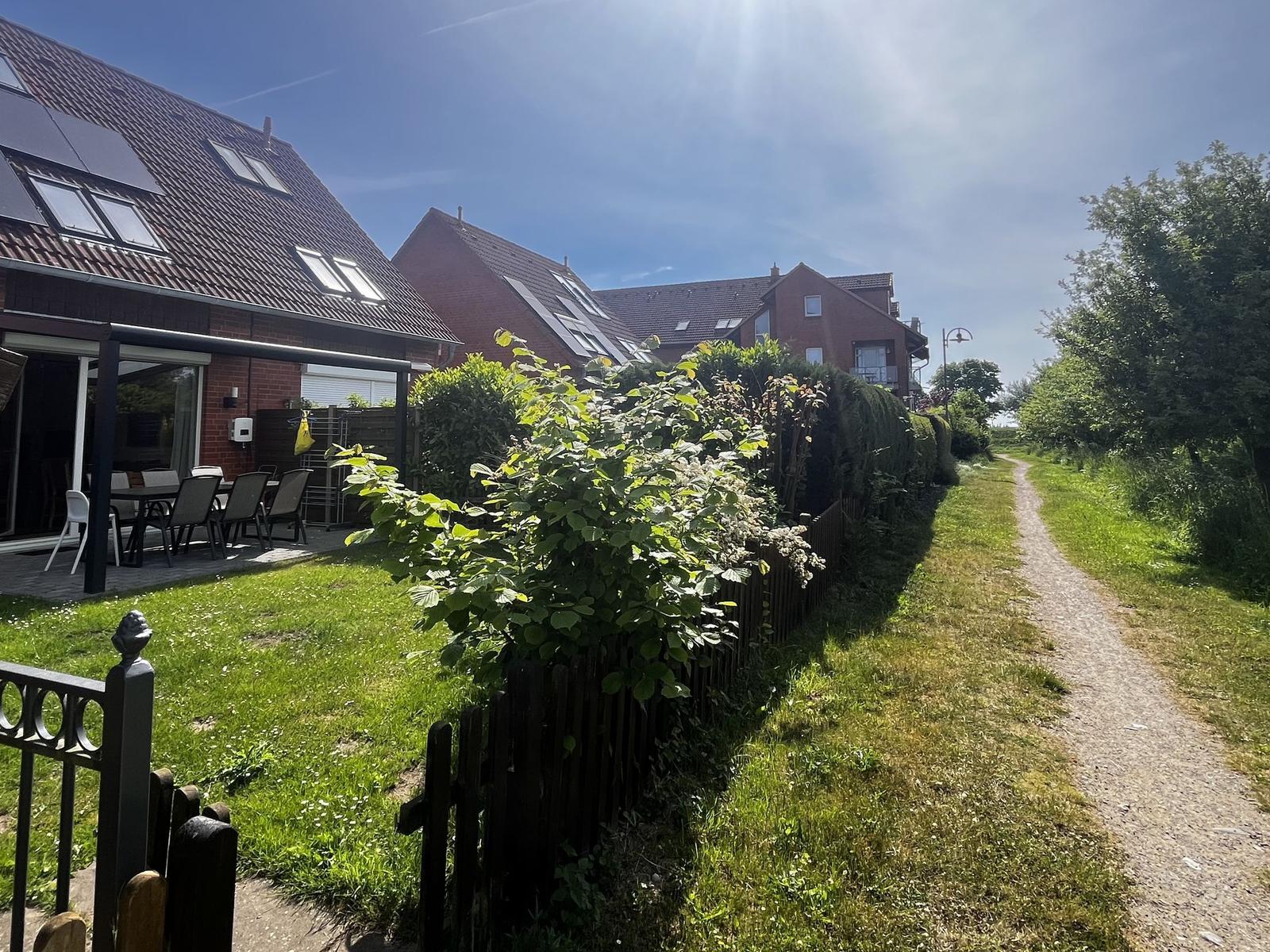 Haus mit Garten, Terrasse und Sonnenschutz. Grünflächen und Weg im Hintergrund.