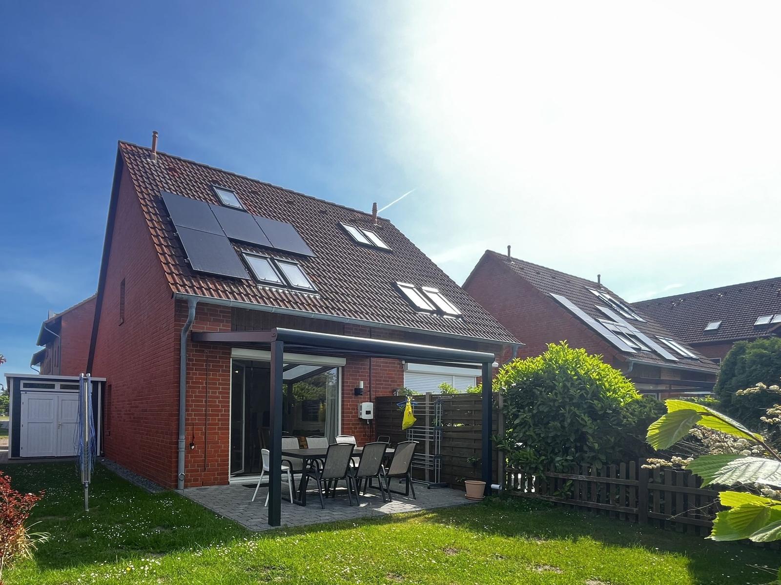 Rotes Backsteinhaus mit Solaranlage und Terrasse mit Tisch und Stühlen.