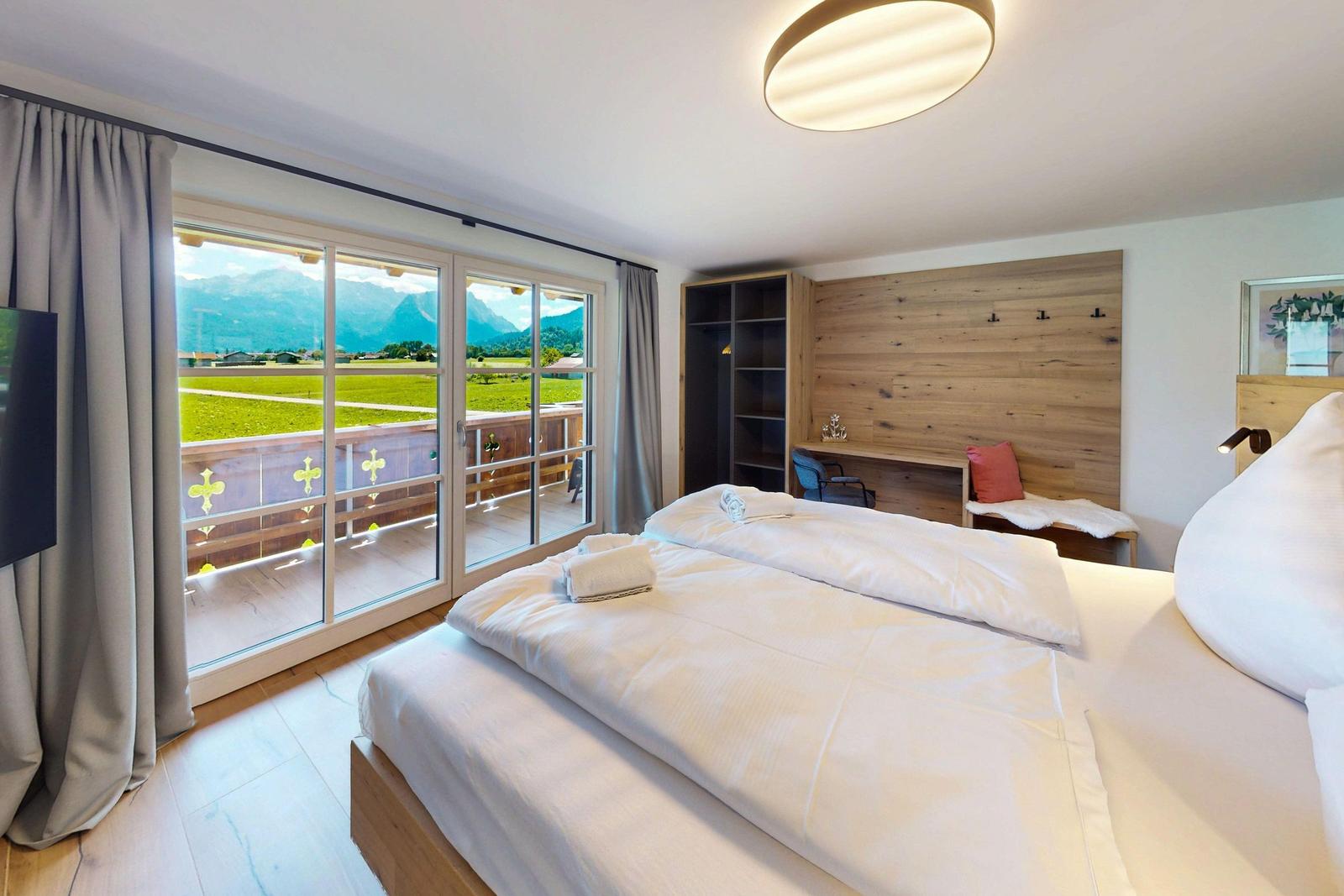 Schlafzimmer mit Balkon und Bergblick. Bett, Schreibtisch und Kleiderständer.