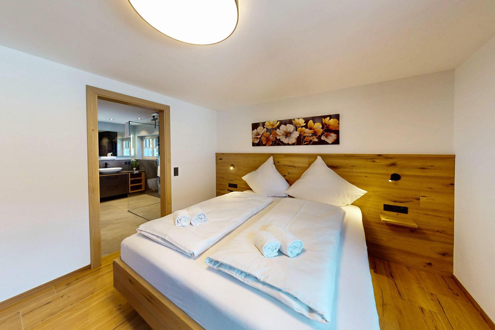 Schlafzimmer mit Holzbett und Bad im Hintergrund.