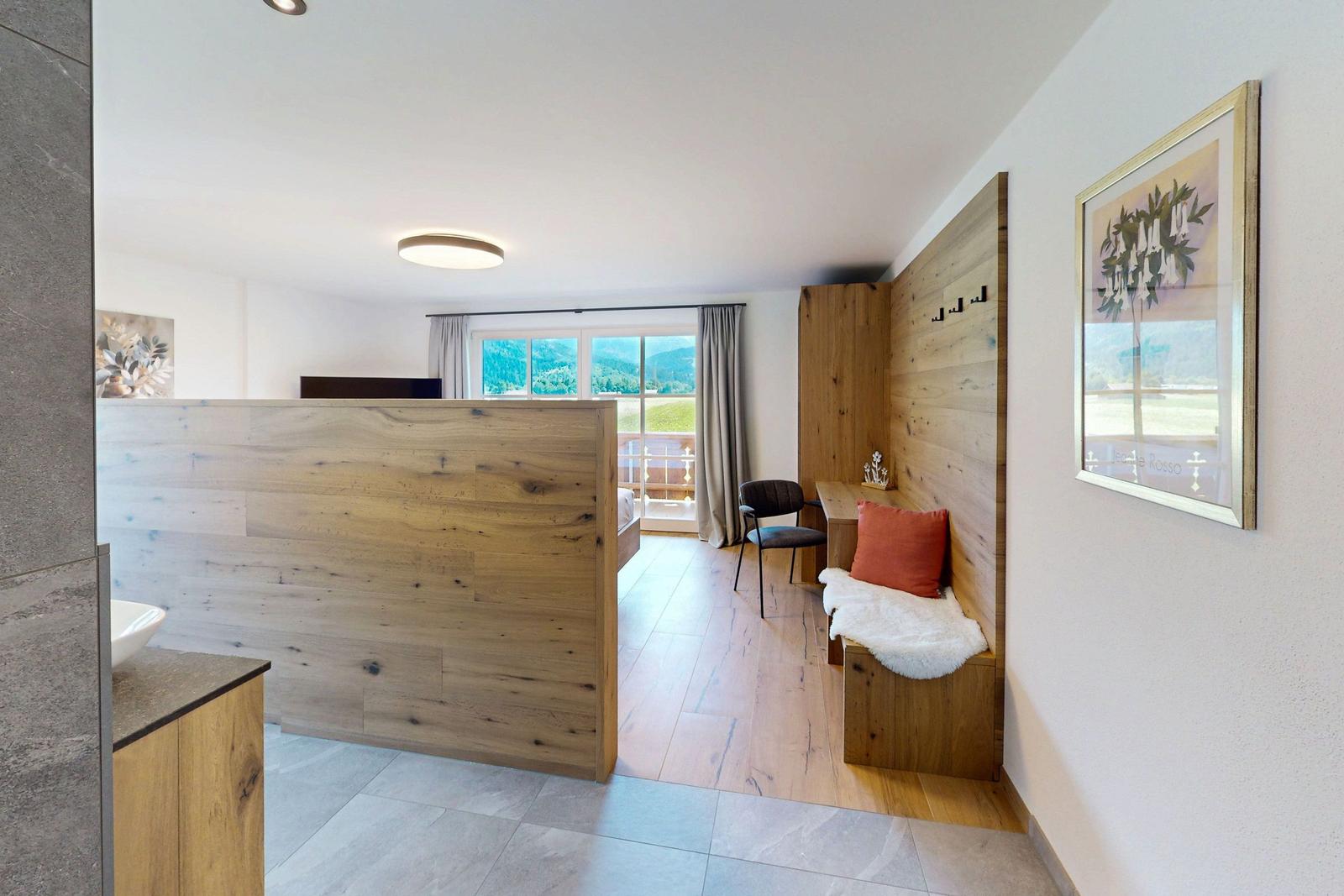 Ein Raum mit Holzwand, Sitzbank, Fenster und Blick auf die Berge.