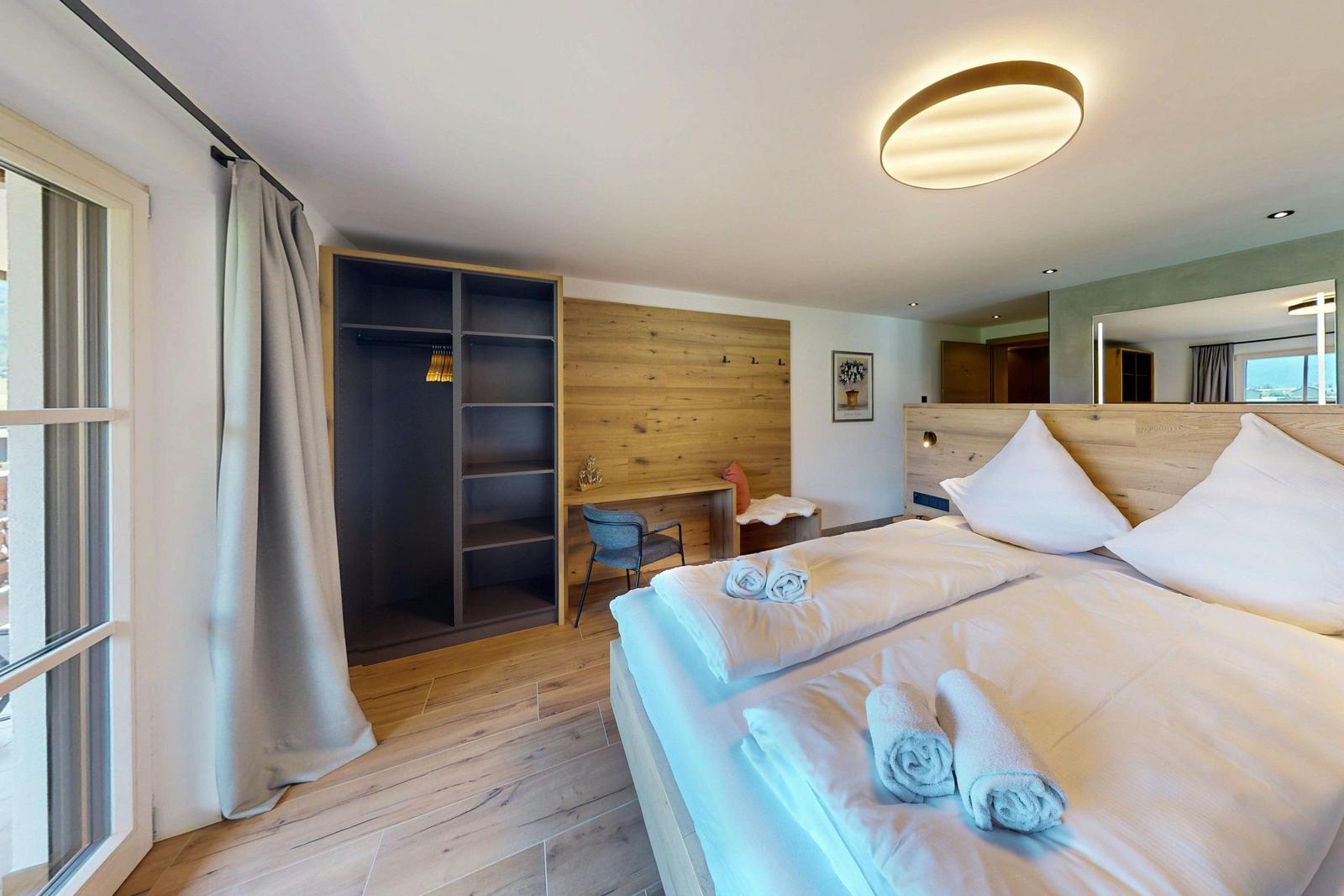 Schlafzimmer mit Doppelbett, Kleiderschrank und Schreibtisch. Holzboden und große Fenster.