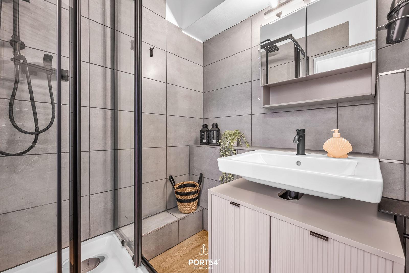 Badezimmer mit Dusche, Waschbecken und Spiegelschrank.