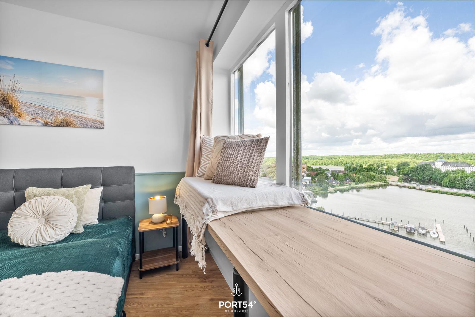 Schlafzimmer mit Blick auf Wasser und Landschaft. Bett, Fensterbank und Wandbild.