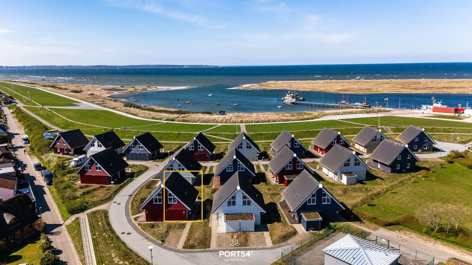 Rotes Haus mit dunklem Dach in einer Wohnanlage am Wasser.
