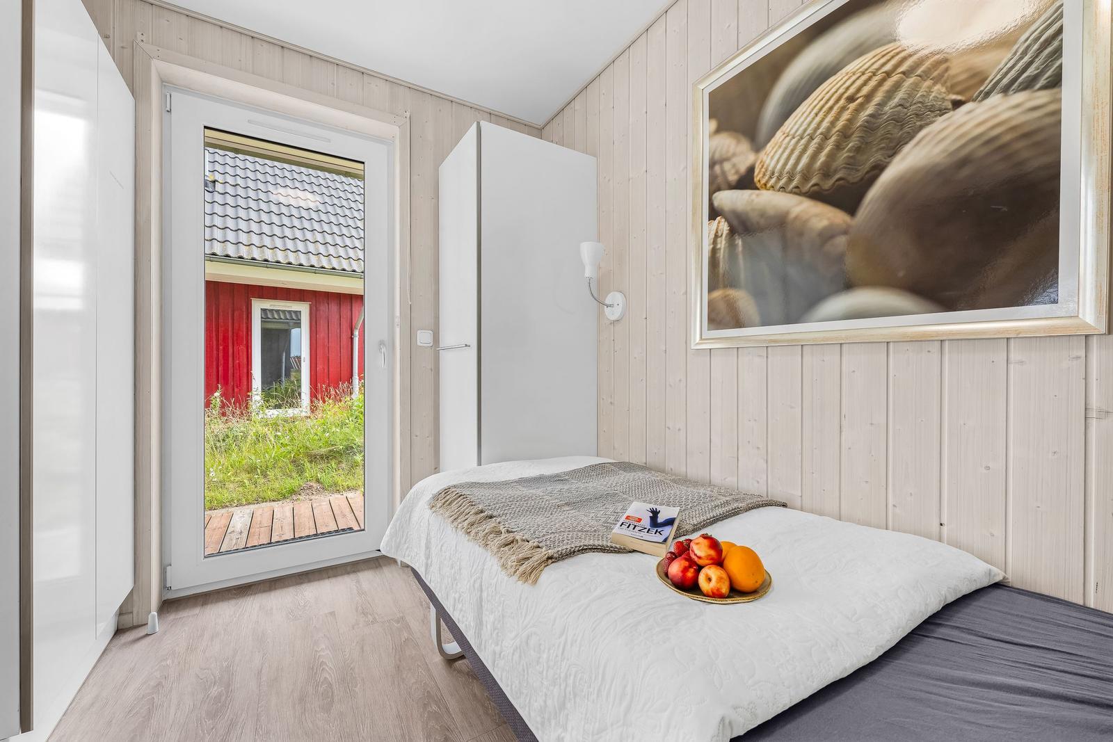 Schlafzimmer mit Bett, Schrank und Tür zum Garten. Wandbild mit Muscheln.