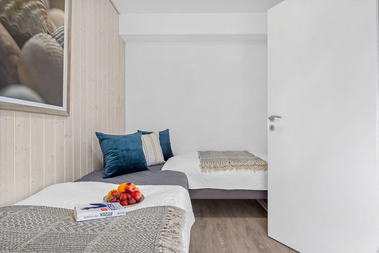 Zwei Betten mit Kissen und Decken, Wandbild mit Muscheln, Tür und Holzboden.