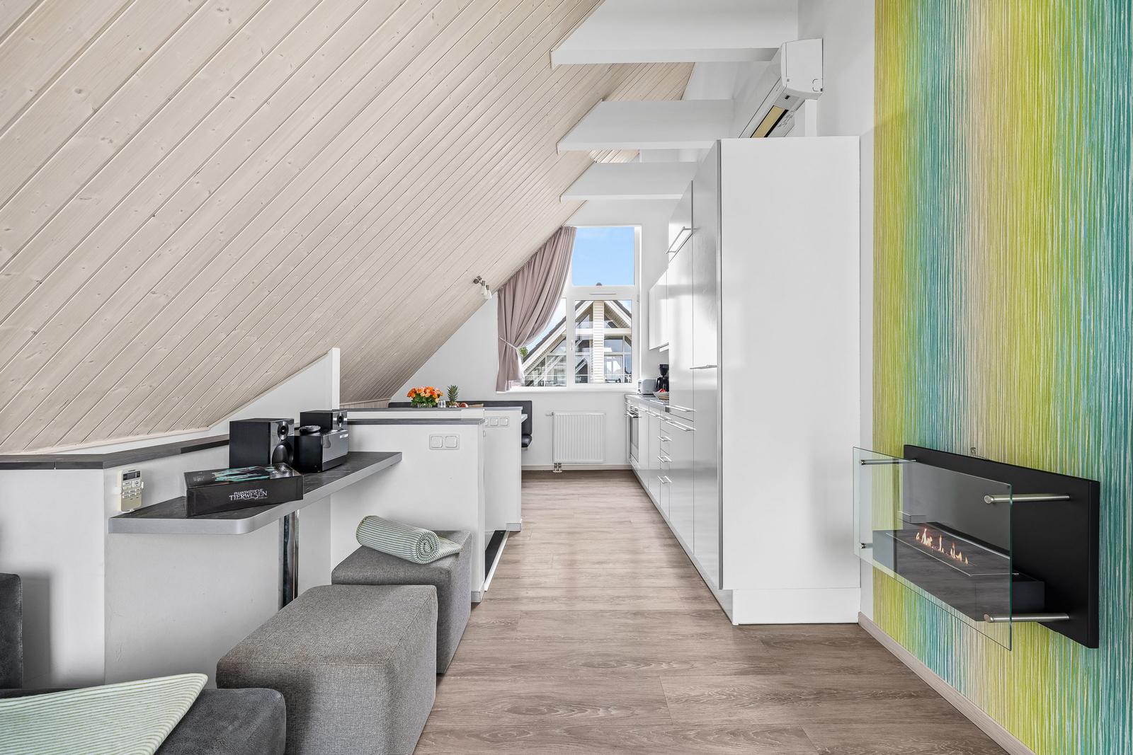 Dachgeschosswohnung mit moderner Küche, Sitzgelegenheiten und Wandkamin.