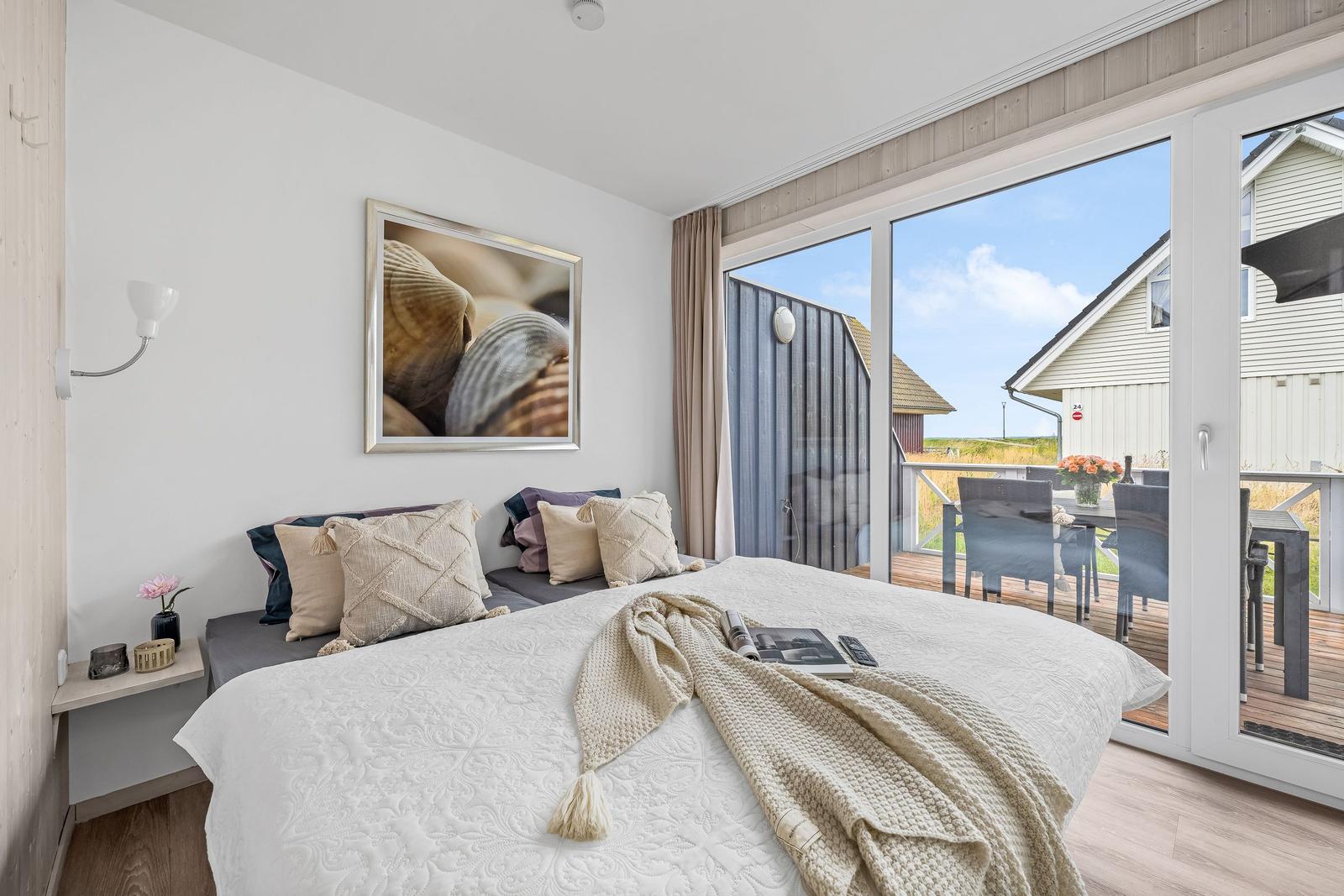 Schlafzimmer mit großem Bett und Blick auf Balkon mit Tisch und Stühlen.