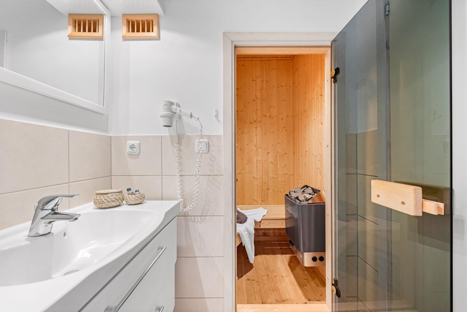 Bad mit Dusche, Waschbecken und Sauna im Hintergrund.