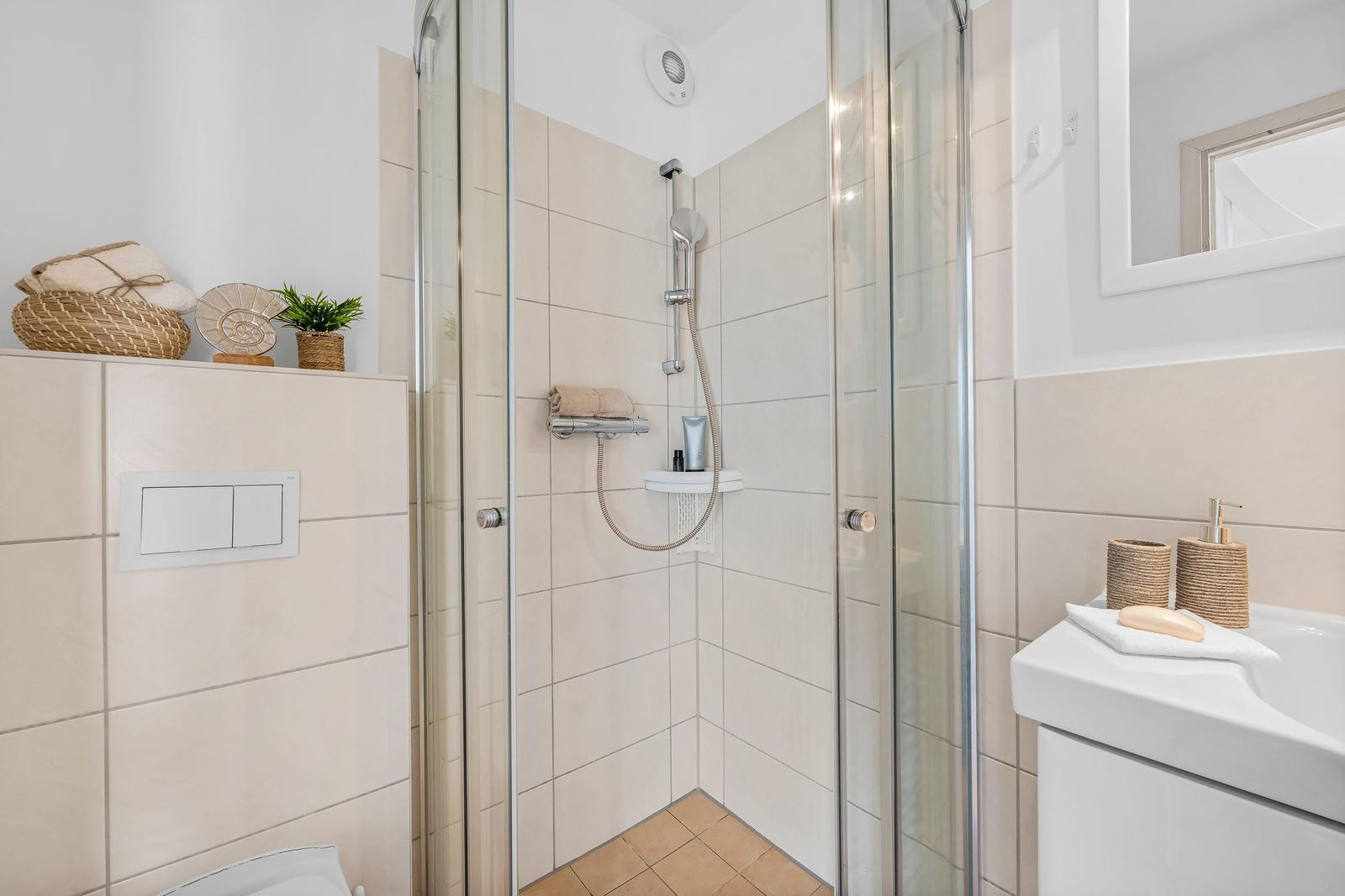 Badezimmer mit Dusche, Waschbecken und Toilette. Weiße Fliesen und Glaswand.