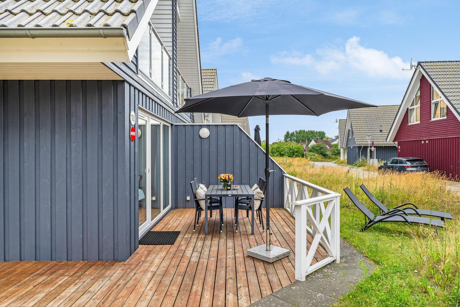 Terrasse mit Tisch, Stühlen und Sonnenschirm neben einem Haus mit Holzverkleidung.