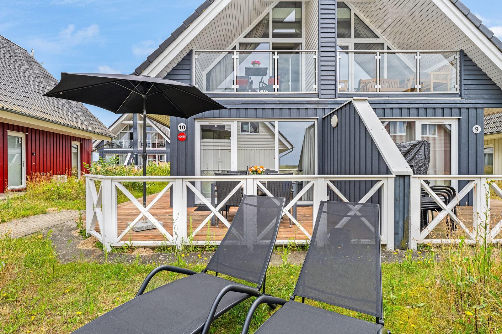 Haus mit Terrasse, Liegestühlen und Sonnenschirm. Zwei Etagen mit Balkon und Fenstern.