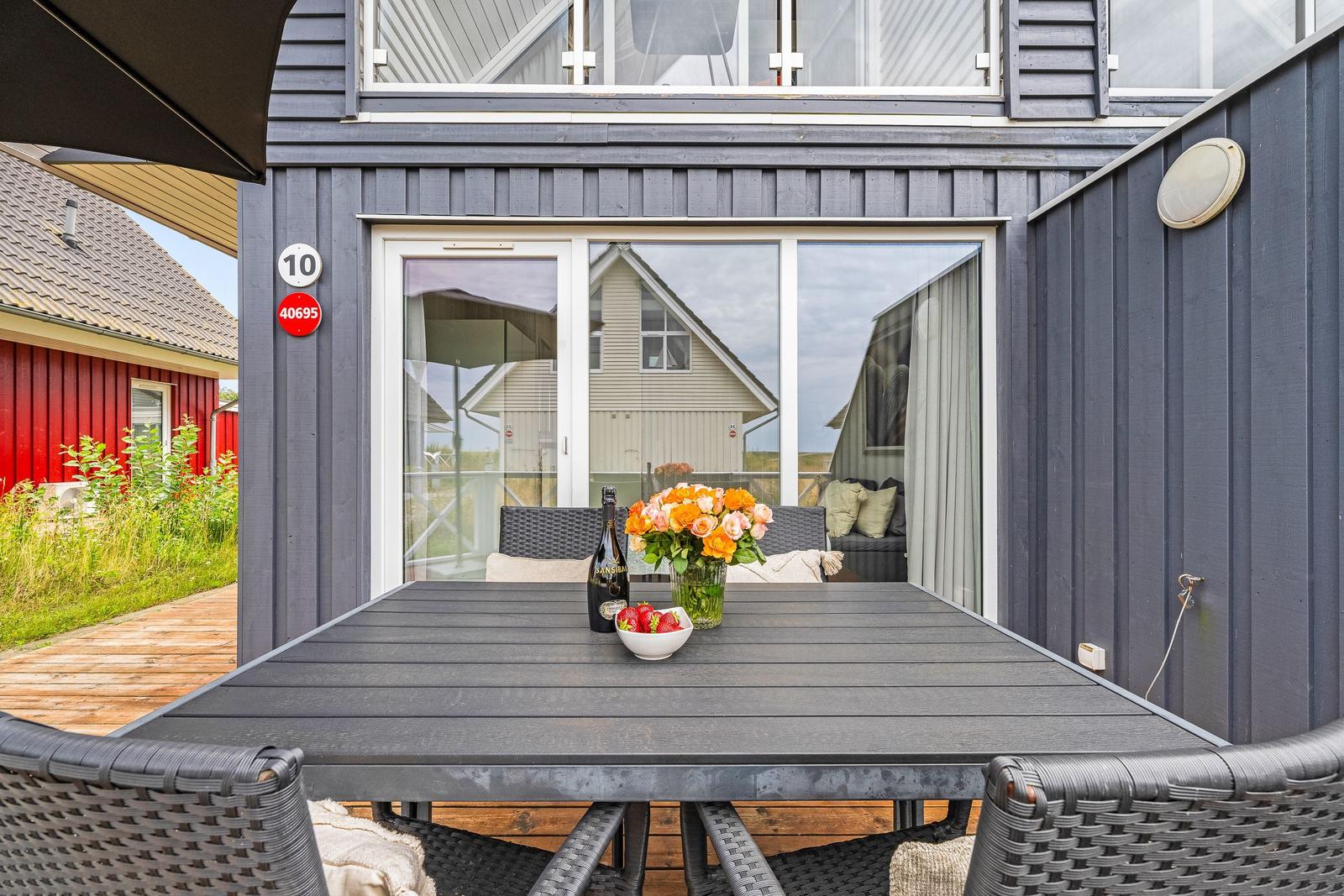 Terrasse mit Tisch, Stühlen und Blumen vor einem Haus mit Glasfront.