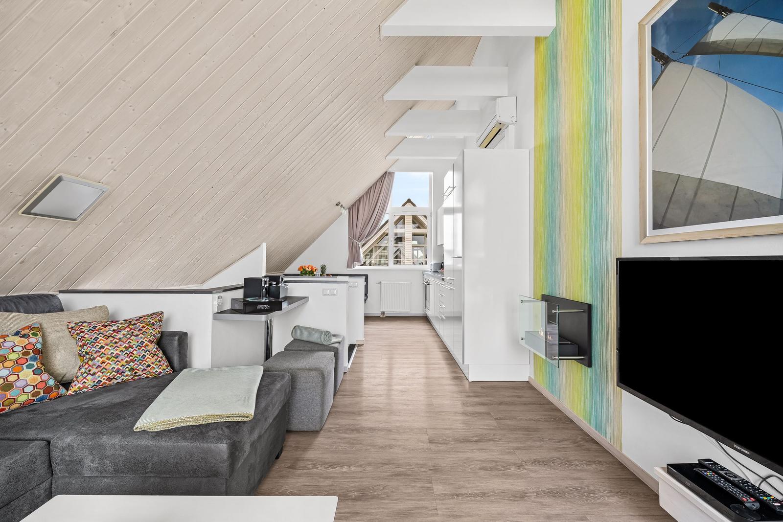 Wohnbereich mit Sofa, Küchenzeile und Fernseher unter schrägem Dach