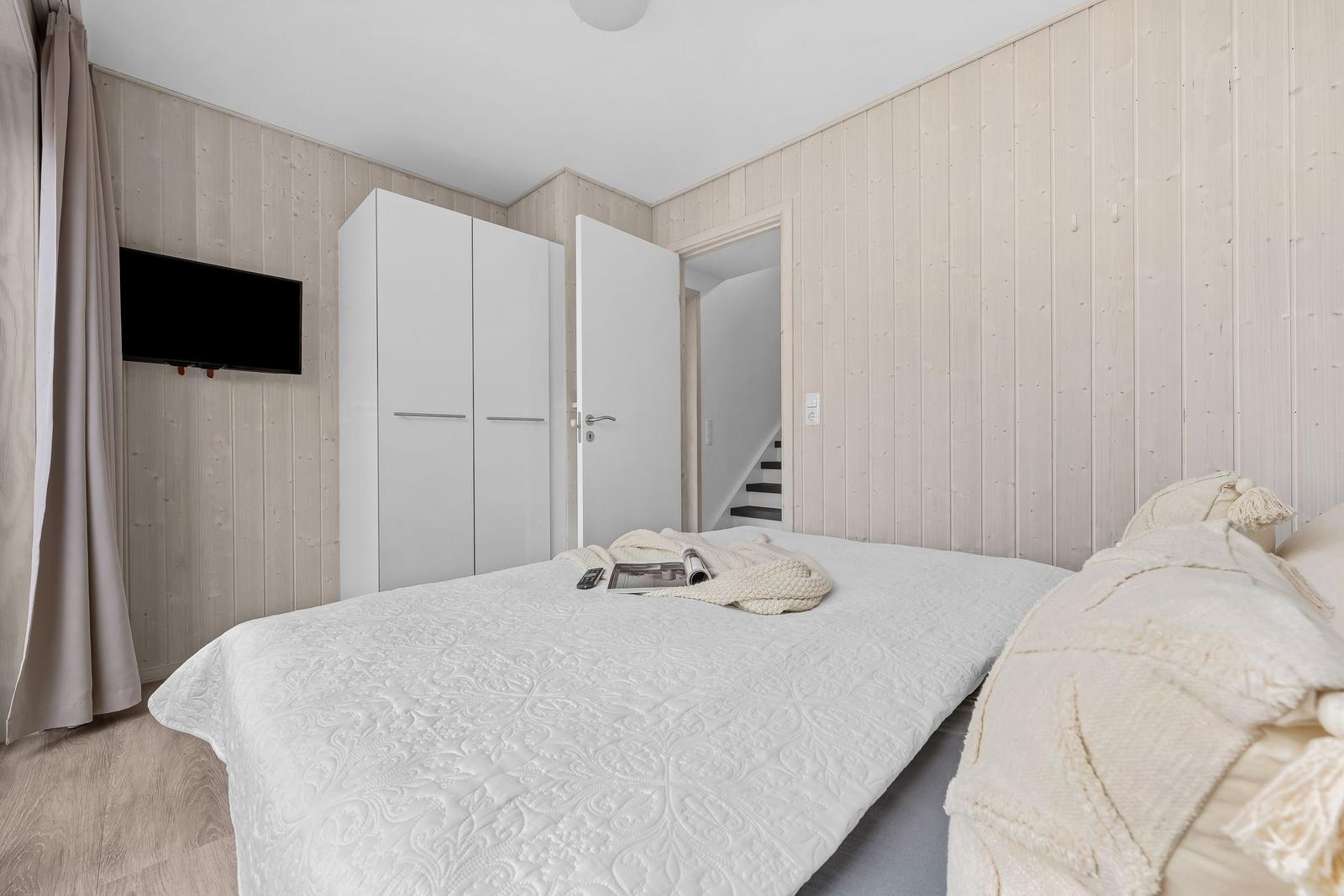 Schlafzimmer mit Bett, Kleiderschrank und Fernseher an der Wand.