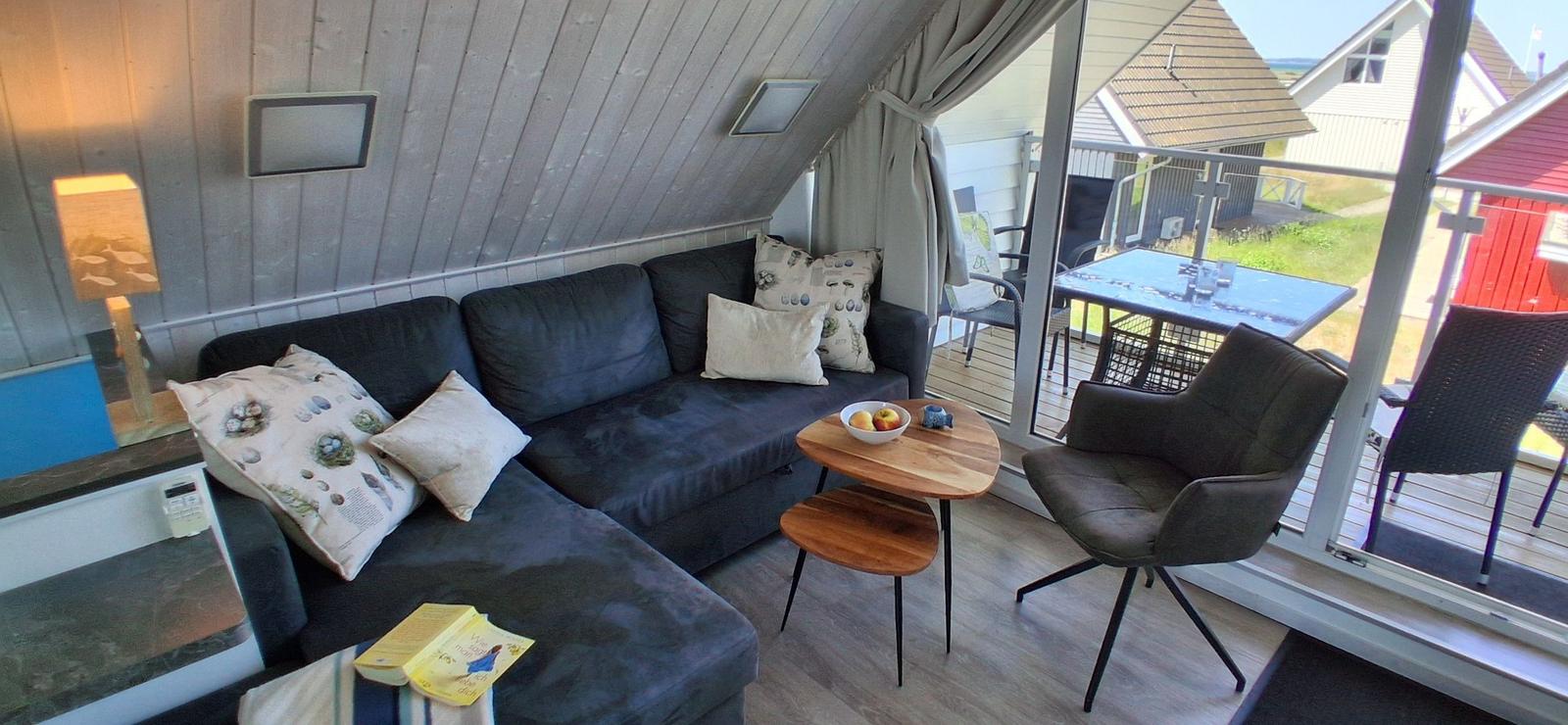 Wohnbereich mit Sofa, Stuhl und Tisch. Durchgang zu Terrasse mit Tisch und Stühlen.