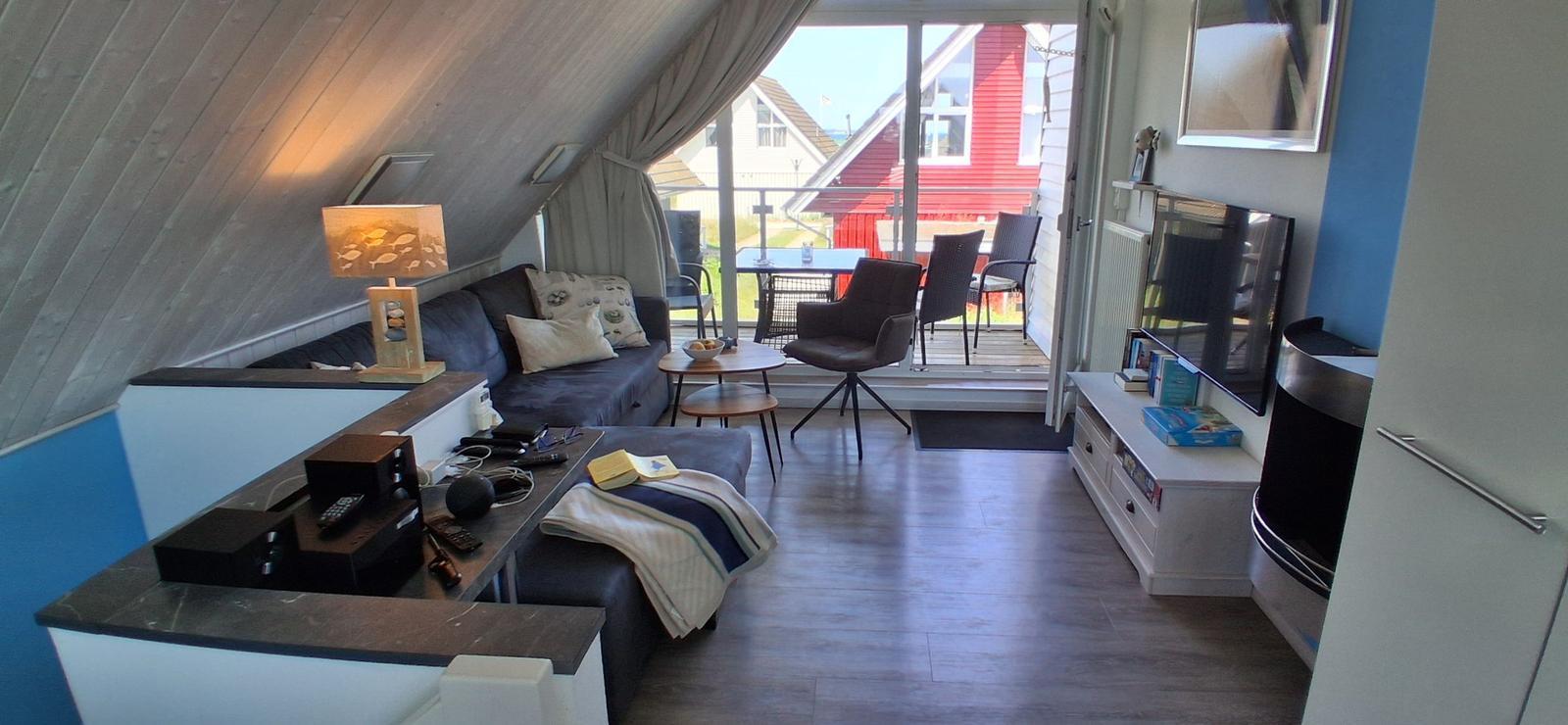 Wohnzimmer mit Sofa, TV und Balkon mit Tisch und Stühlen.