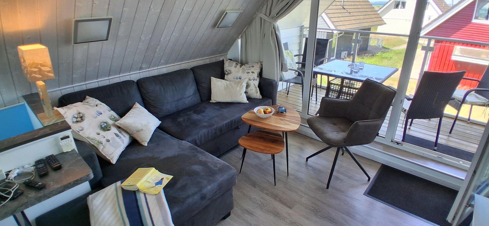Wohnbereich mit Sofa, Stuhl und Tisch. Durchgang zur Terrasse mit Tisch und Stühlen.