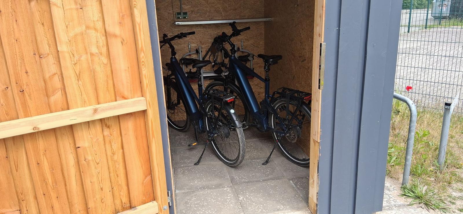 Zwei E-Bikes stehen in einem Holzschuppen mit Betonboden.