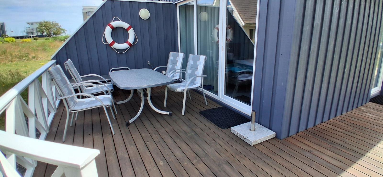 Terrasse mit Tisch und Stühlen, Rettungsring an Wand, Holzdecke und Glastür.