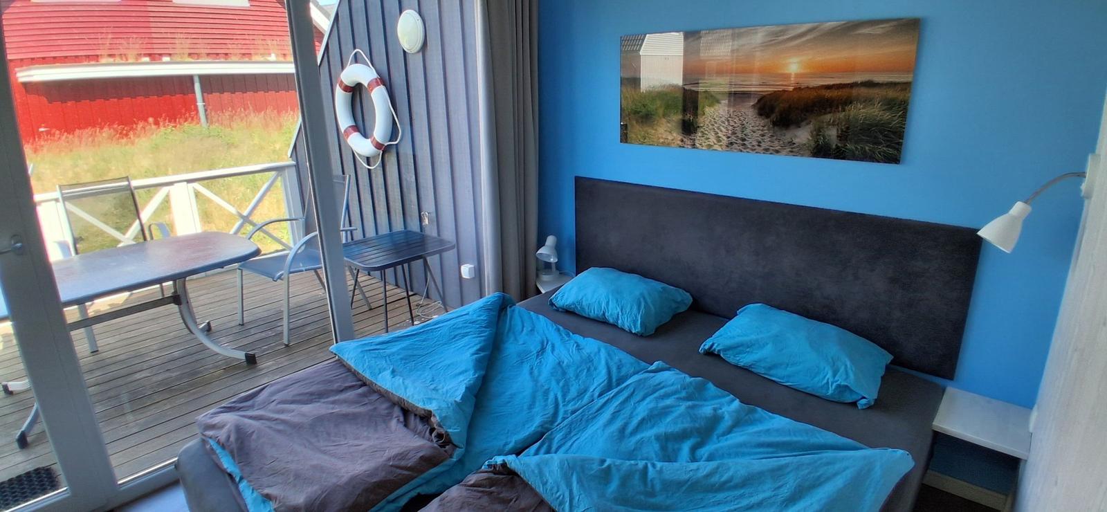 Schlafzimmer mit Bett, blauer Wand und Balkon mit Tisch und Stühlen.