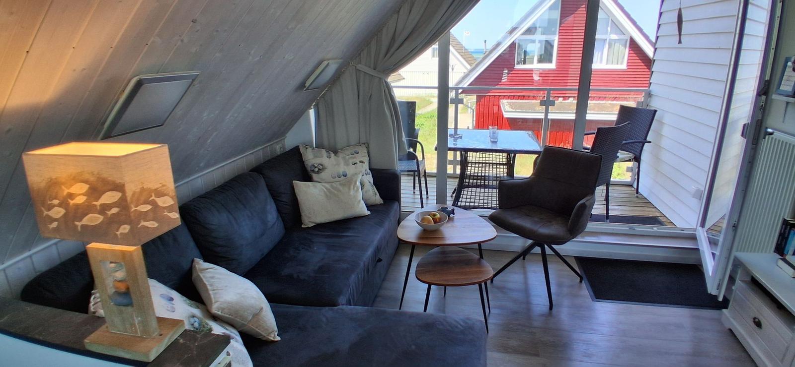 Wohnbereich mit Sofa, Stuhl und Tisch. Durchgang zur Terrasse mit Tisch und Stühlen.