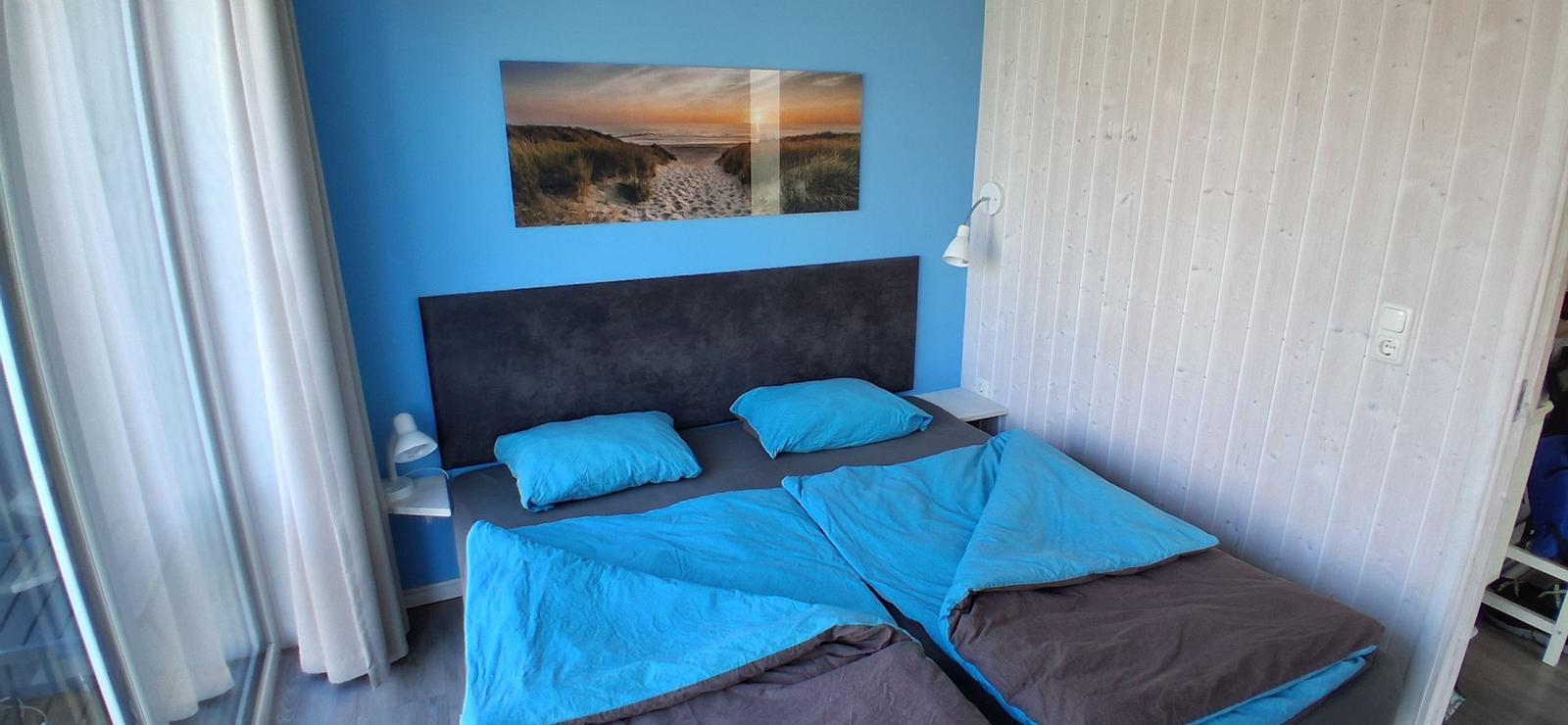 Schlafzimmer mit Bett, Wandbild und weißen Lampen.