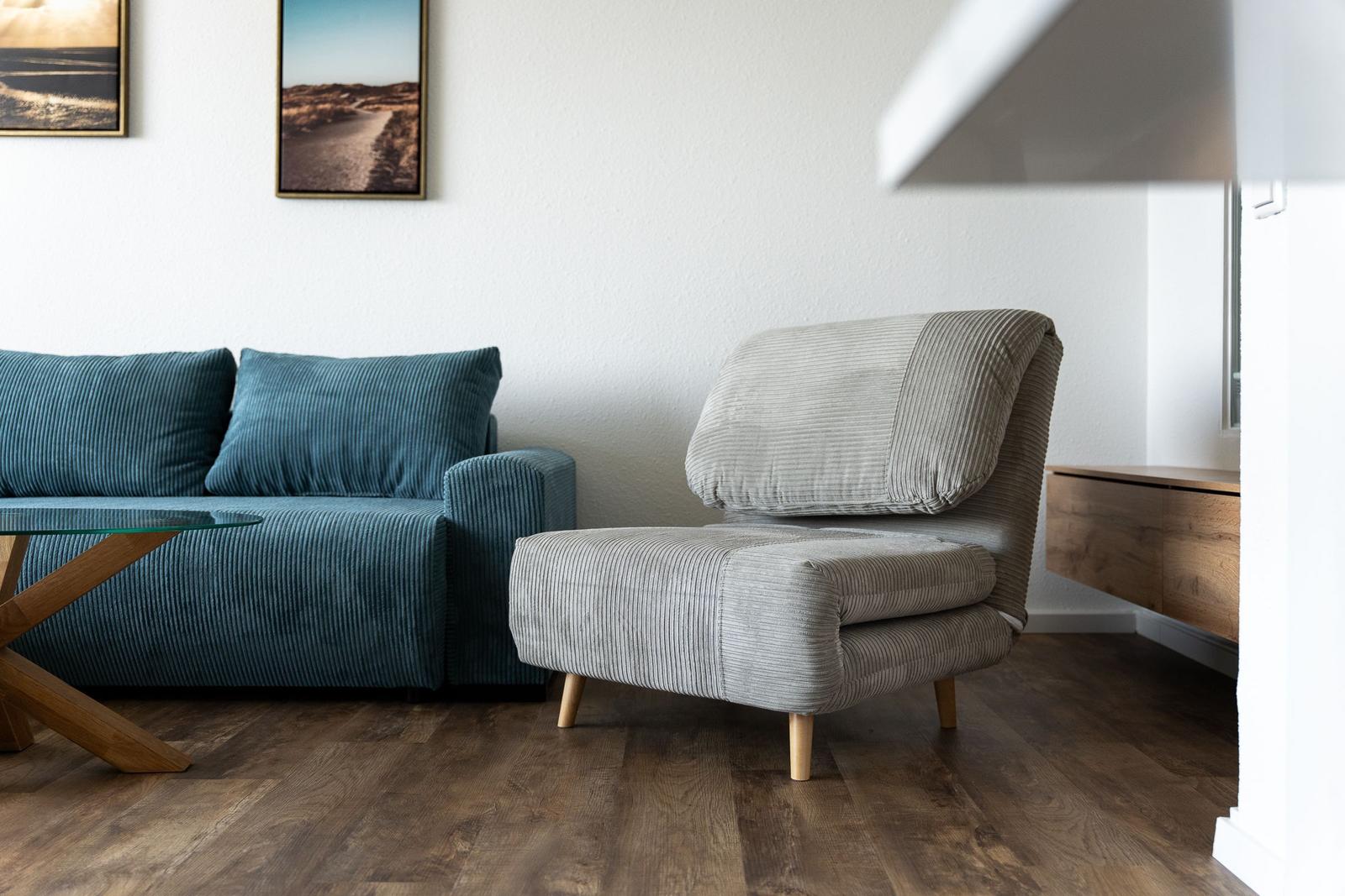 Ein Raum mit blauem Sofa und grauem Sessel auf Holzboden.