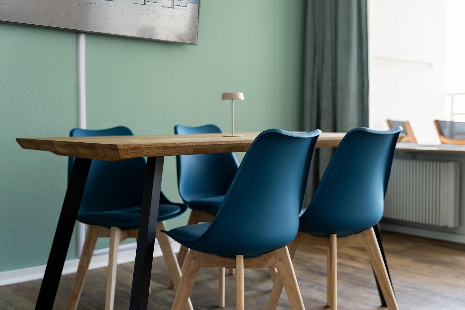 Holztisch mit vier blauen Stühlen und einer Lampe auf der Tischplatte.