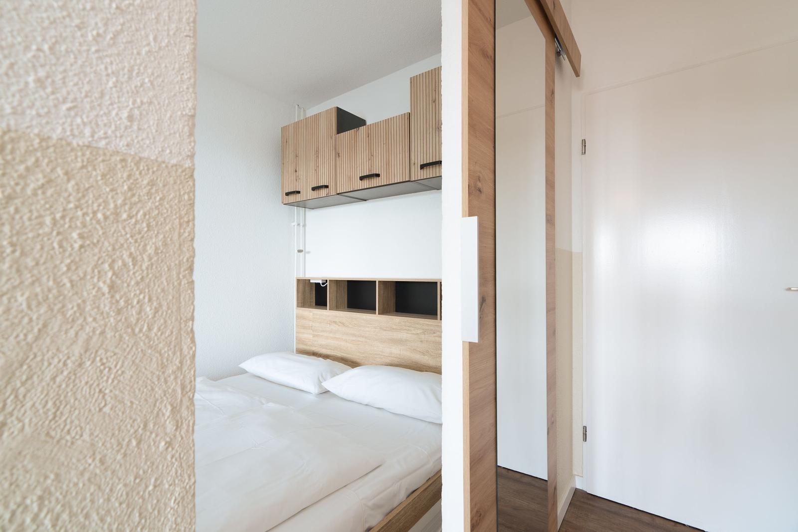 Schlafzimmer mit Bett, Holzmöbel und Schrank. Blick durch Türöffnung.
