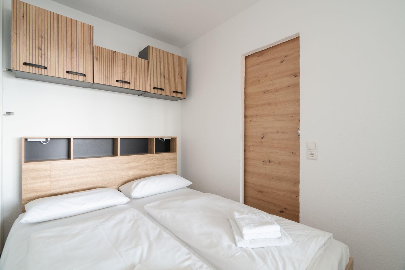 Schlafzimmer mit Bett, Holzregalen und Tür.
