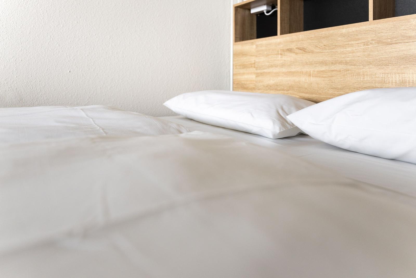 Doppelbett mit weißer Bettwäsche und Holzkopfteil.