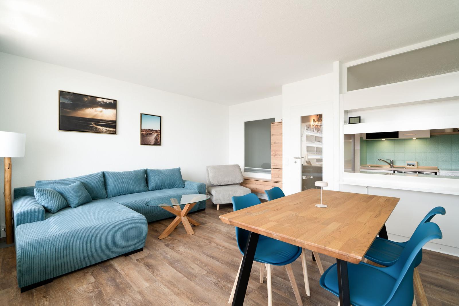 Wohn- und Essbereich mit blauem Sofa, Holztisch und Küchenbereich.