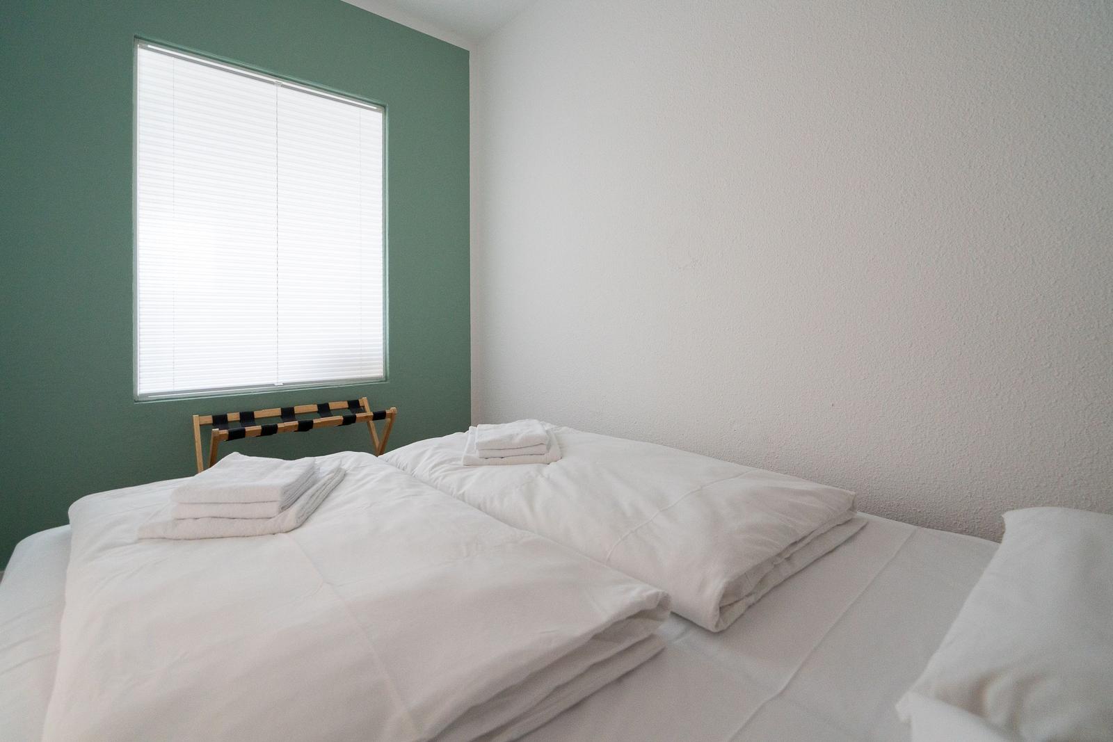 Schlafzimmer mit weißem Bett, grüner Wand und Fenster mit Jalousie.