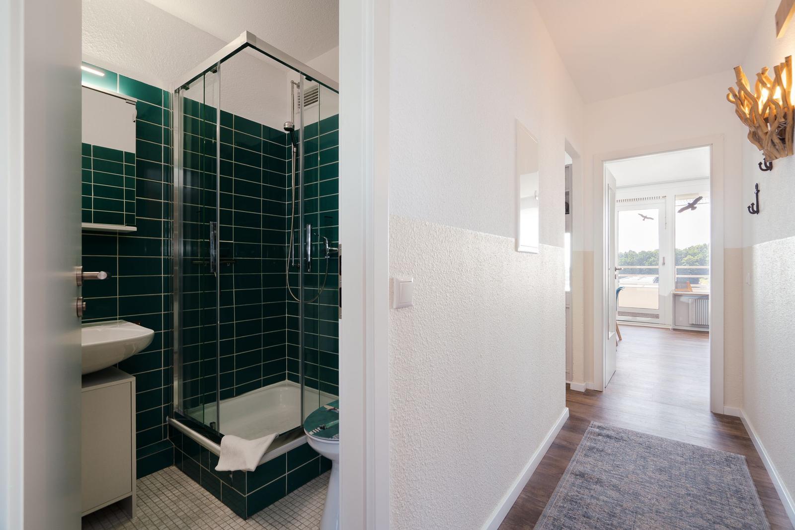 Badezimmer mit Dusche und Toilette. Flur führt zum Balkon.