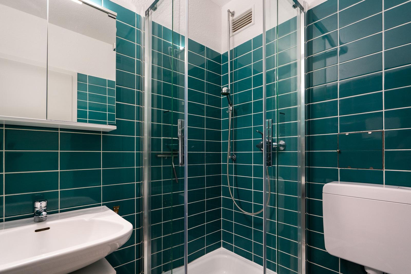 Badezimmer mit Dusche, Waschbecken und Toilette. Wandfliesen in Türkis.