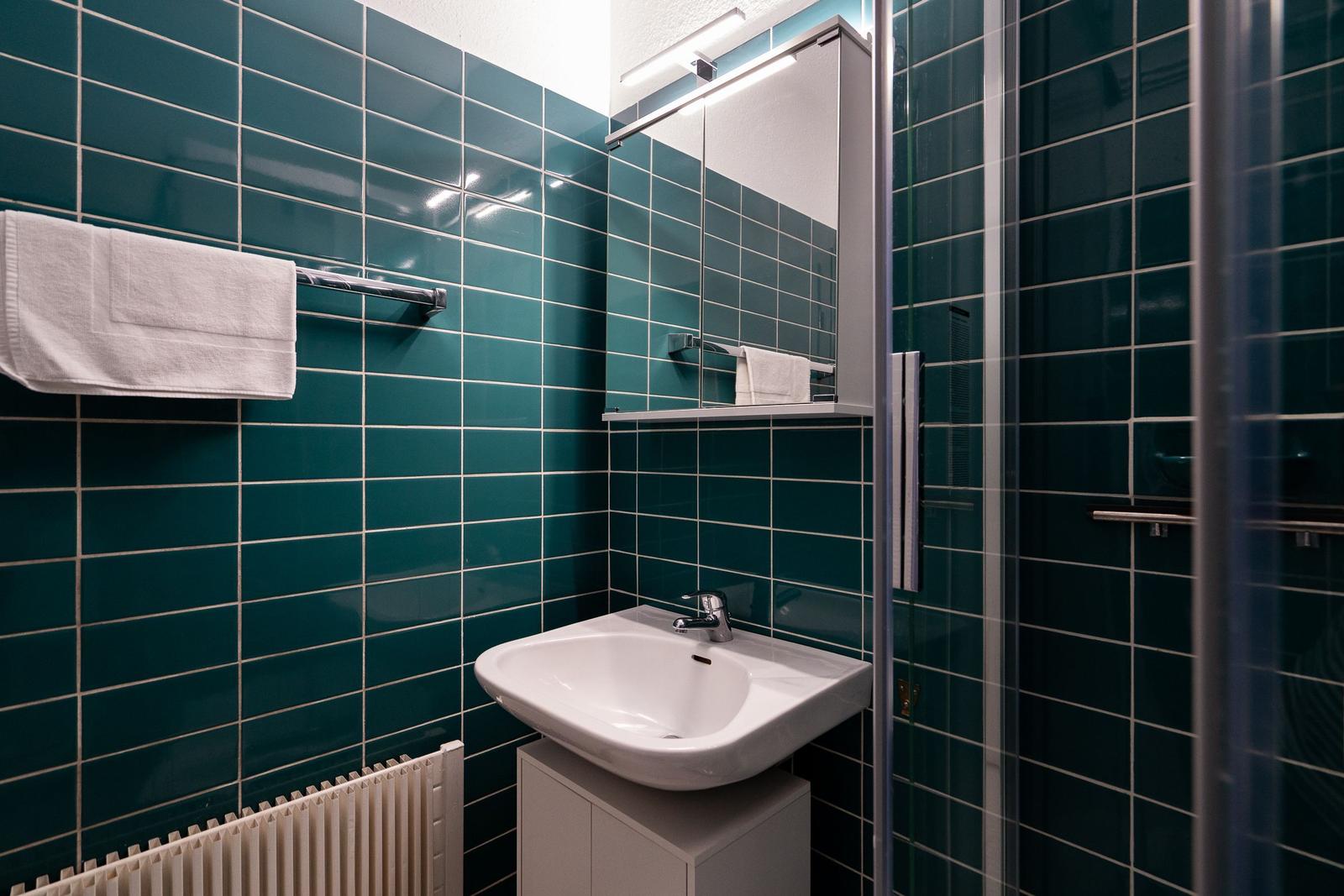 Badezimmer mit grünen Fliesen, Waschbecken, Spiegel und Dusche.