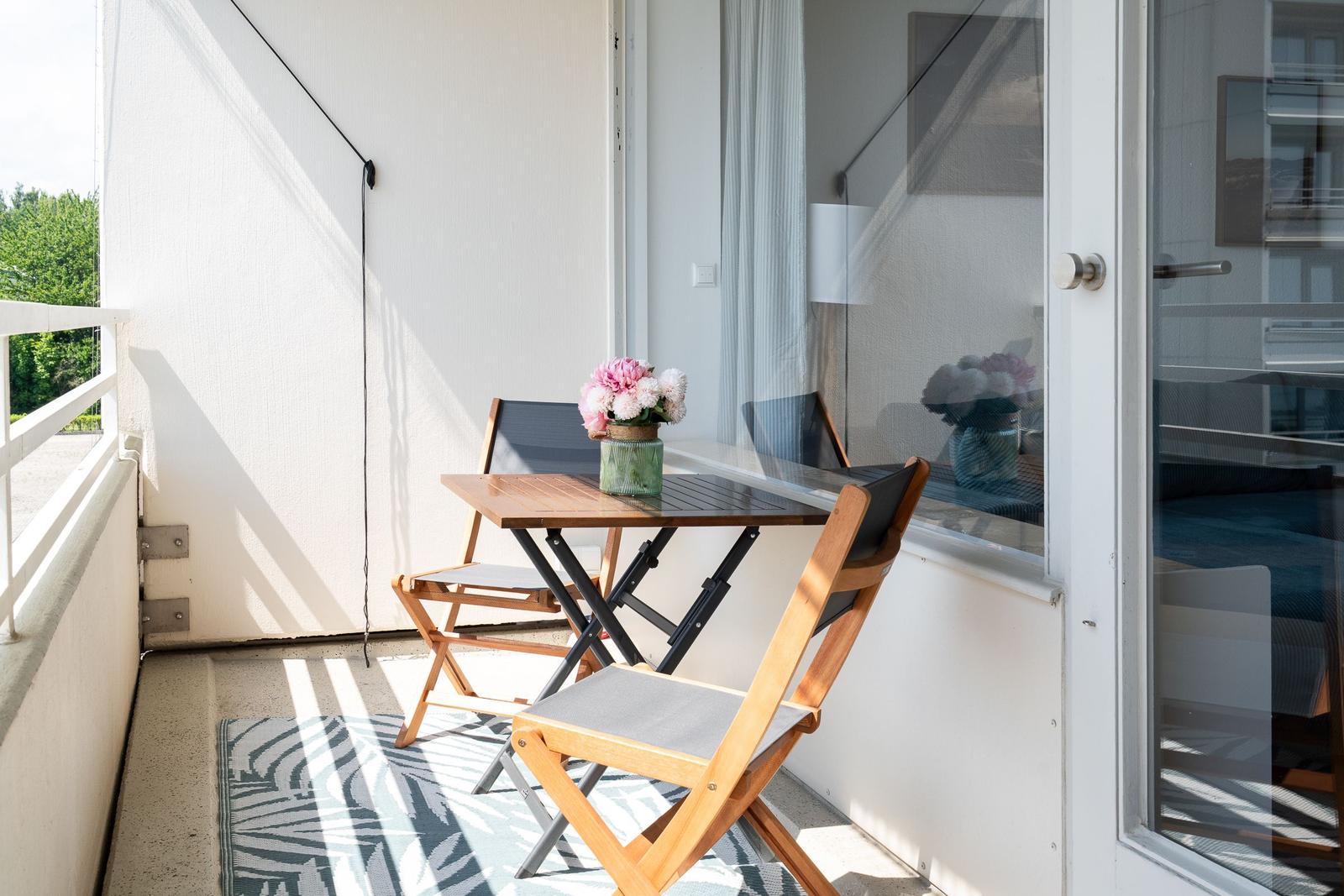 Terrasse mit Tisch, zwei Stühlen und Blumenarrangement. Durchgang zur Wohnung.