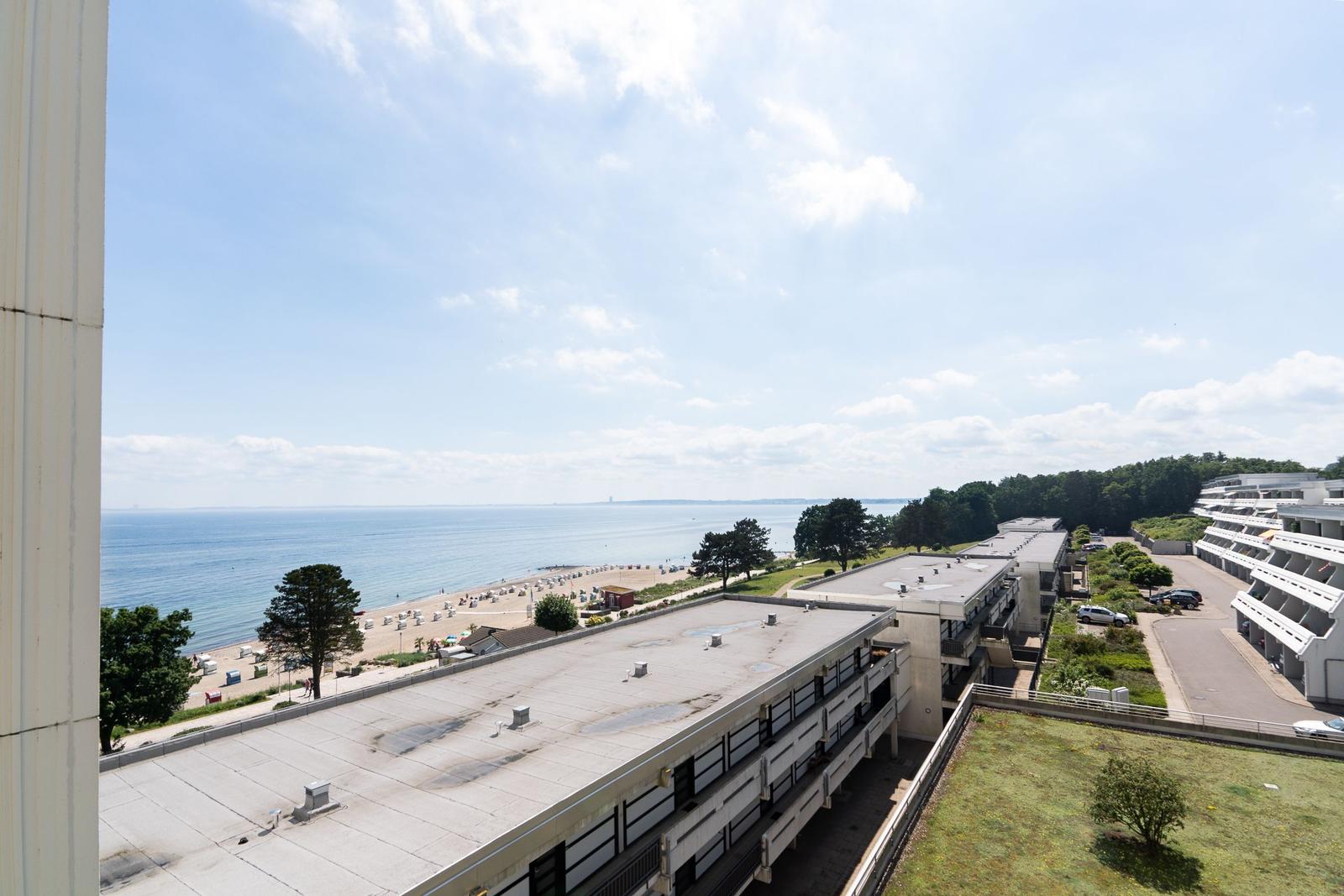 Blick auf Strand und Meer mit mehrstöckigen Gebäuden und grüner Fläche.