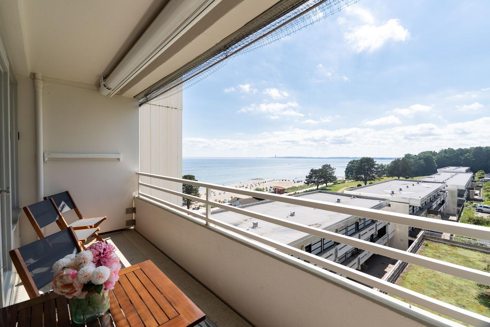 Balkon mit Tisch, Stühlen und Blumen. Blick auf Strand und Meer.