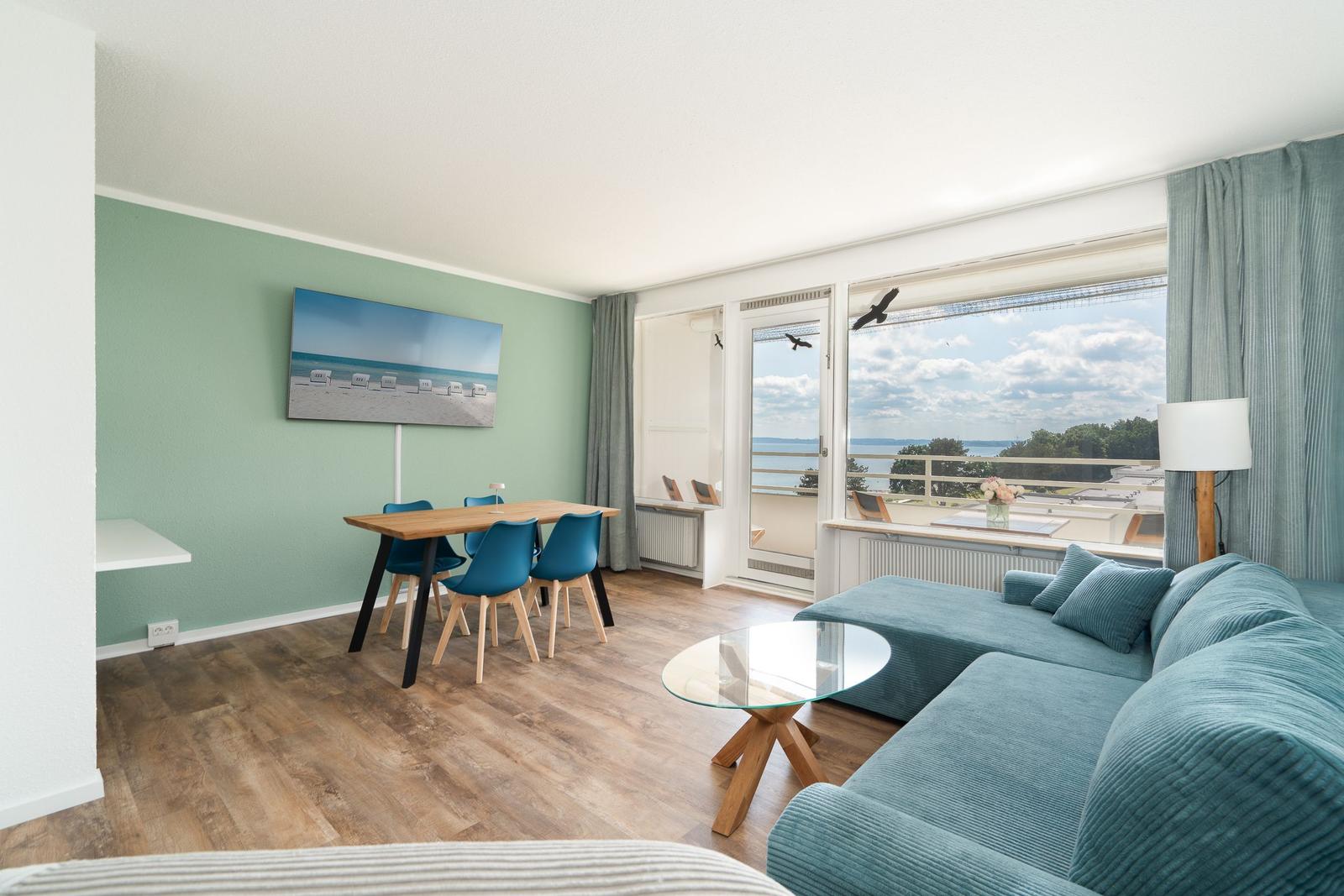 Wohnzimmer mit Sofa, Esstisch und Balkonblick auf Wasser