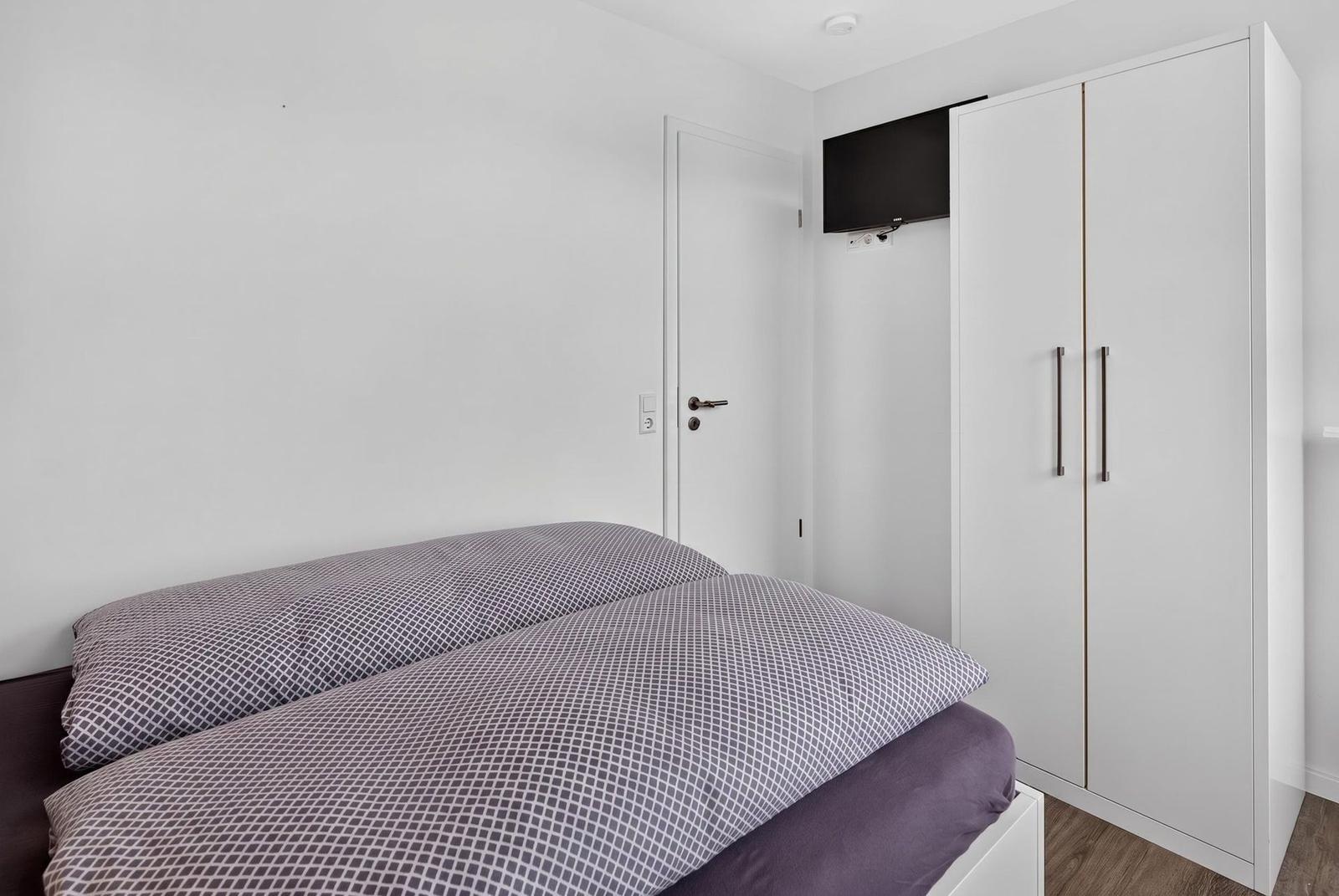 Schlafzimmer mit Bett, Kleiderschrank und Wandfernseher.