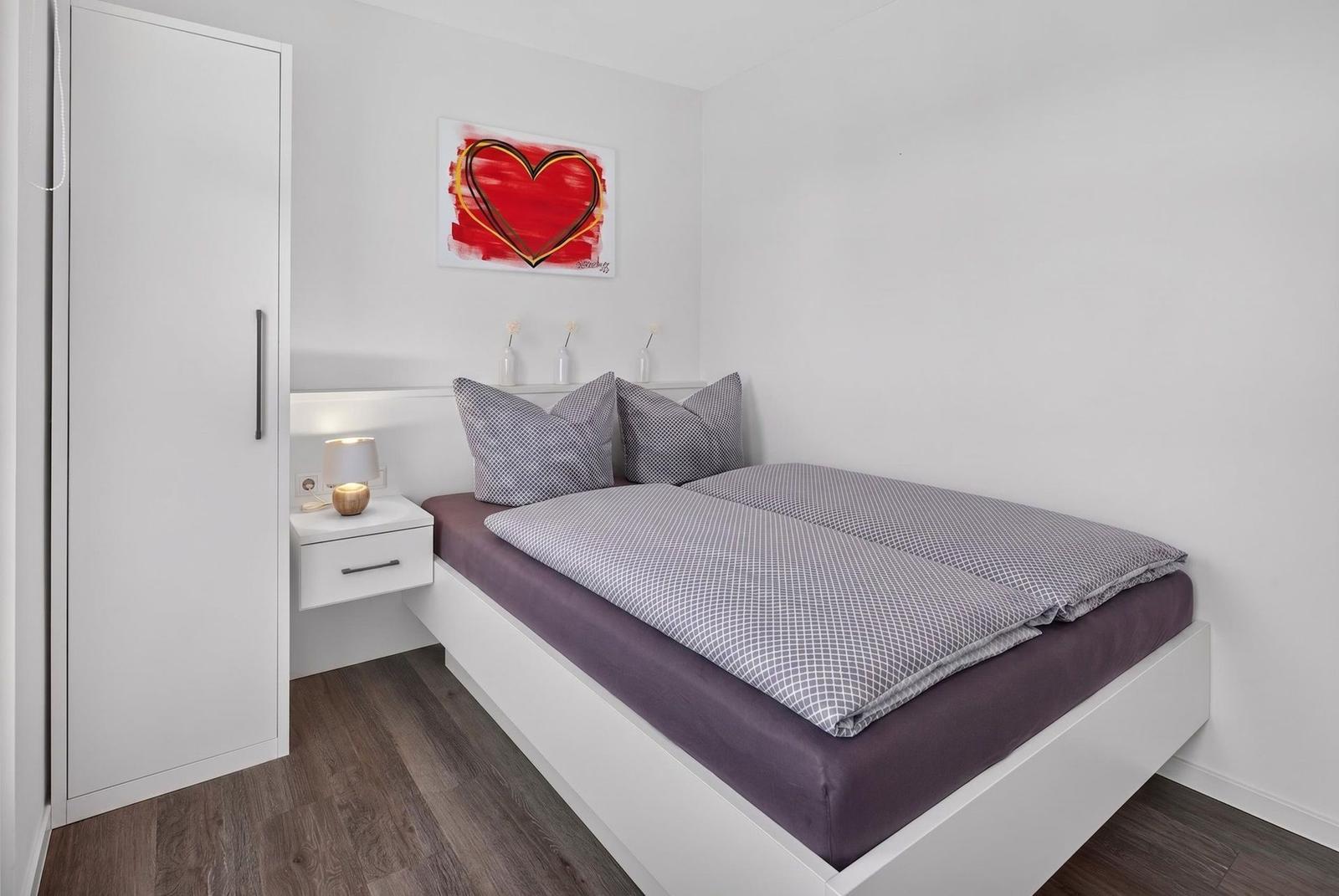 Schlafzimmer mit Bett, Nachttisch und Kleiderschrank. Wandbild mit Herz.