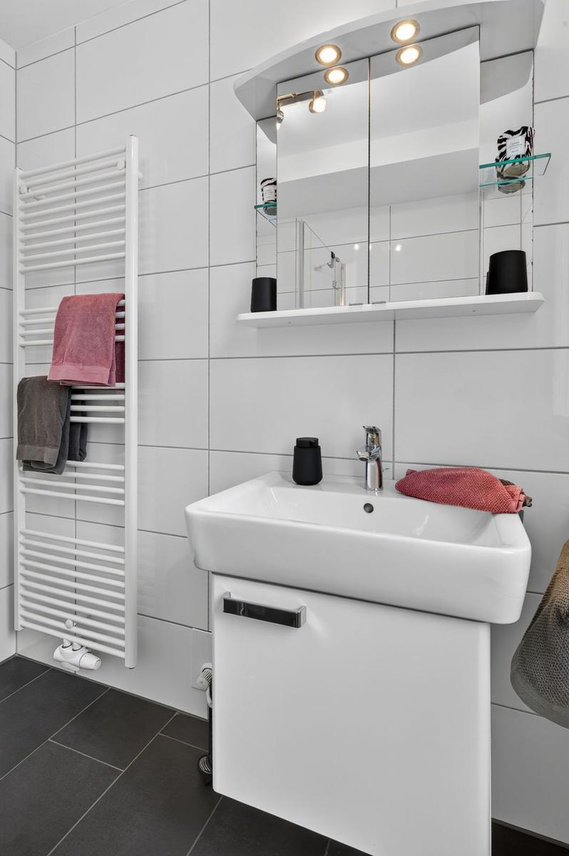 Bad mit Waschbecken, Spiegelschrank und Heizkörper mit Handtüchern.