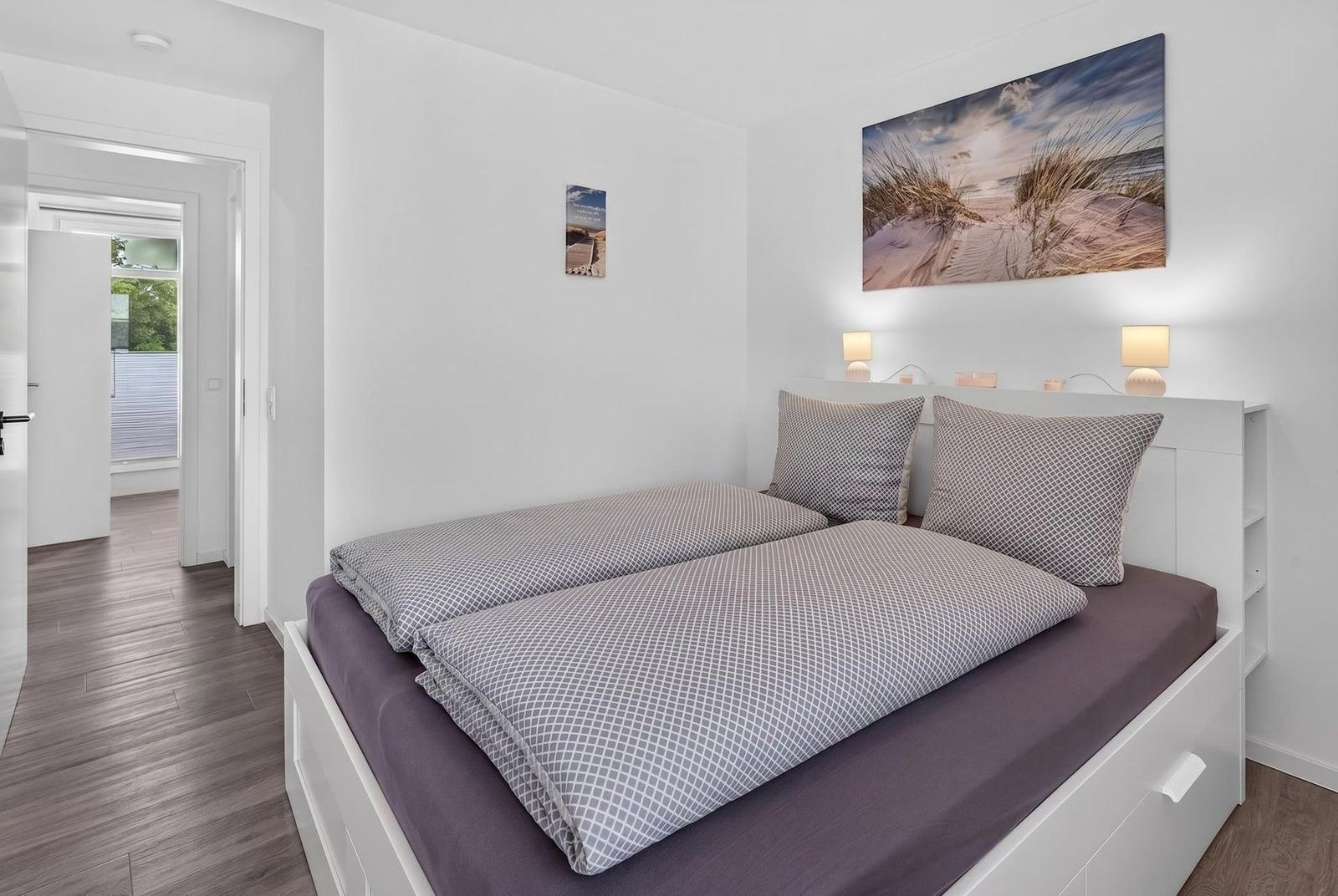 Schlafzimmer mit Bett, Wandbild und Nachttischlampen. Durchgang zu angrenzenden Räumen.